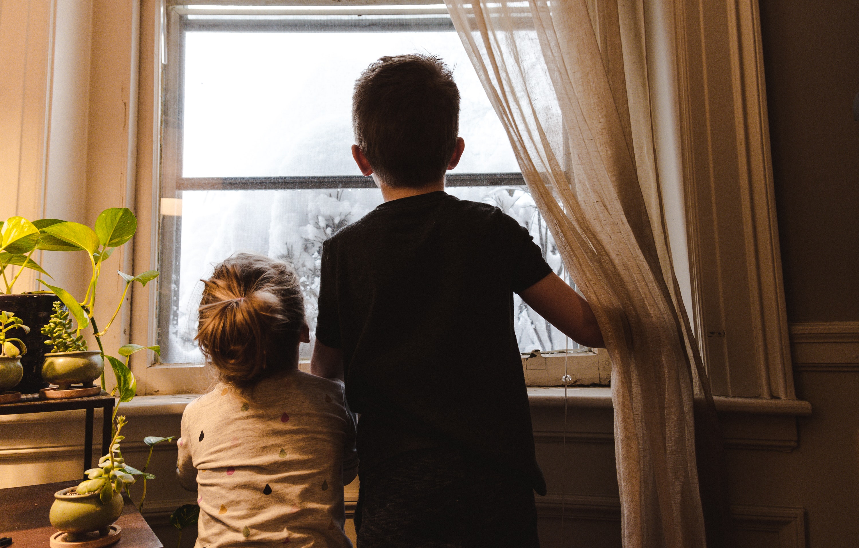 Två barn står och tittar ut i ett fönster